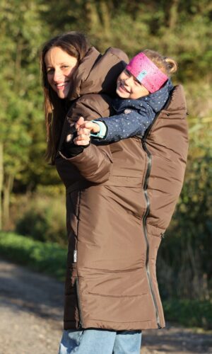 maminka nese velkou smějící se holčičku na zádech v nosící hnědé bundě zn. Angel Wings