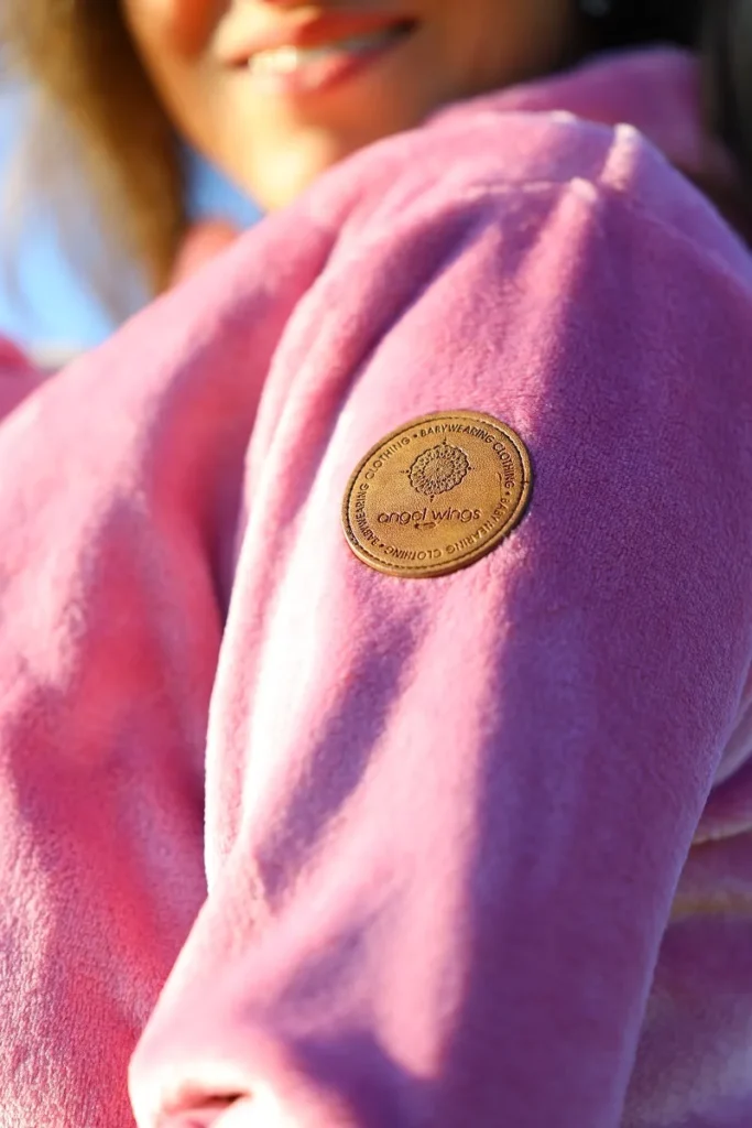 Detailní pohled na kožené logo Angel Wings na rukávu růžové nosící mikiny z fleecu.